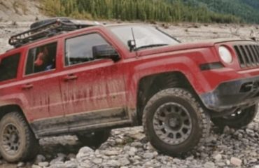 Lifted red Jeep Patriot with Mud tires off-road on rocky cliff