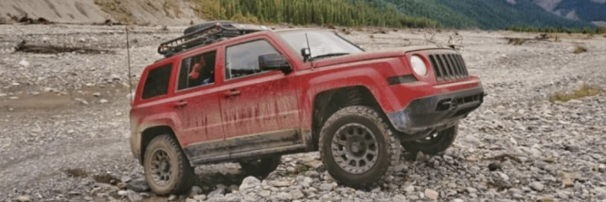 Lifted red Jeep Patriot with Mud tires off-road on rocky cliff