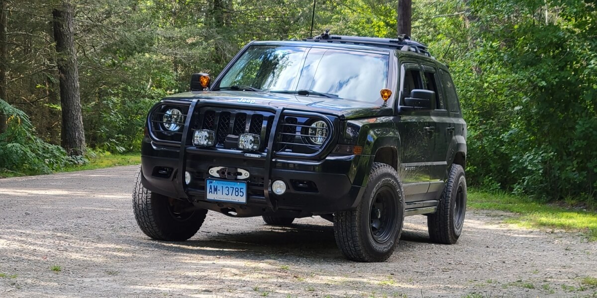Black Jeep Patriot equipped with off-road bumper, lights and mud tires