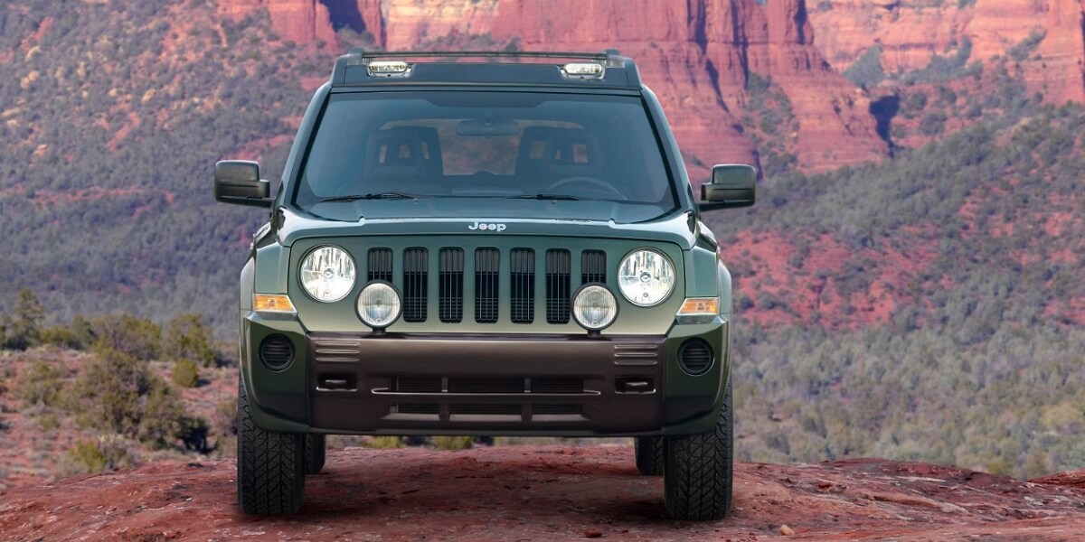 Khaki Jeep Patriot standing in front of red mountains and green woods