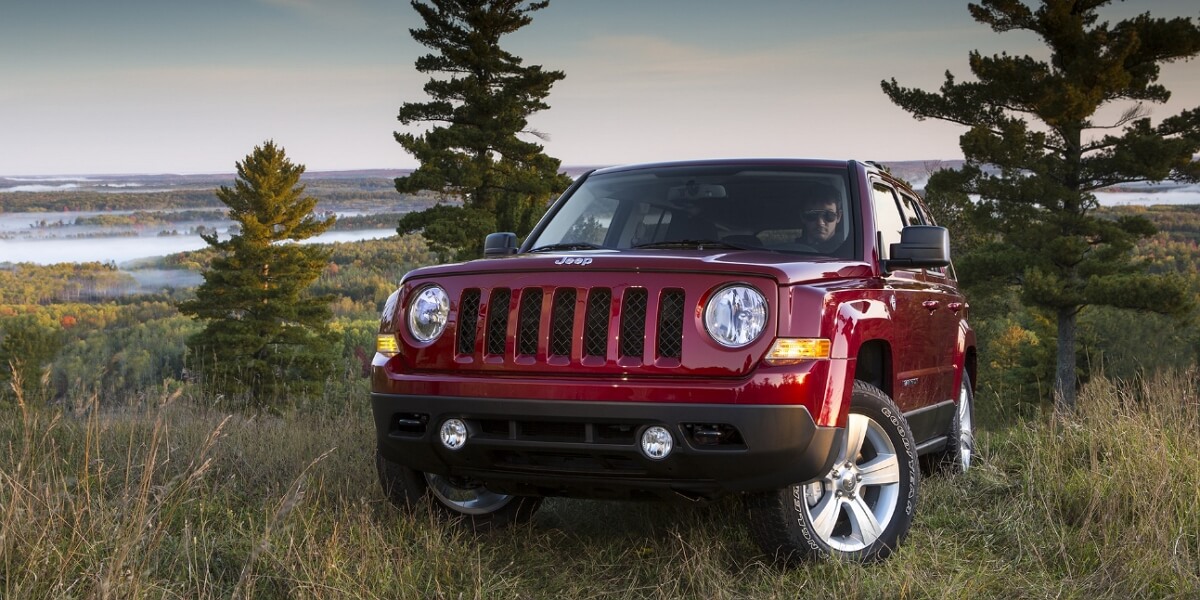 Red Jeep Patriot gone off-road on woody landscape background